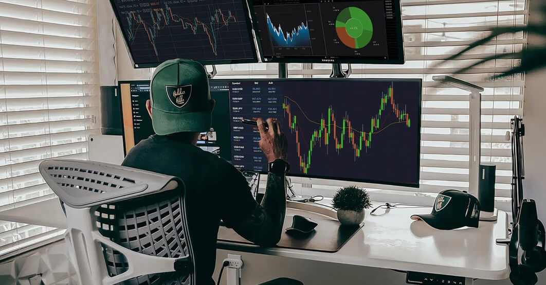 A man is analysing market data across four screens filled with trading information.