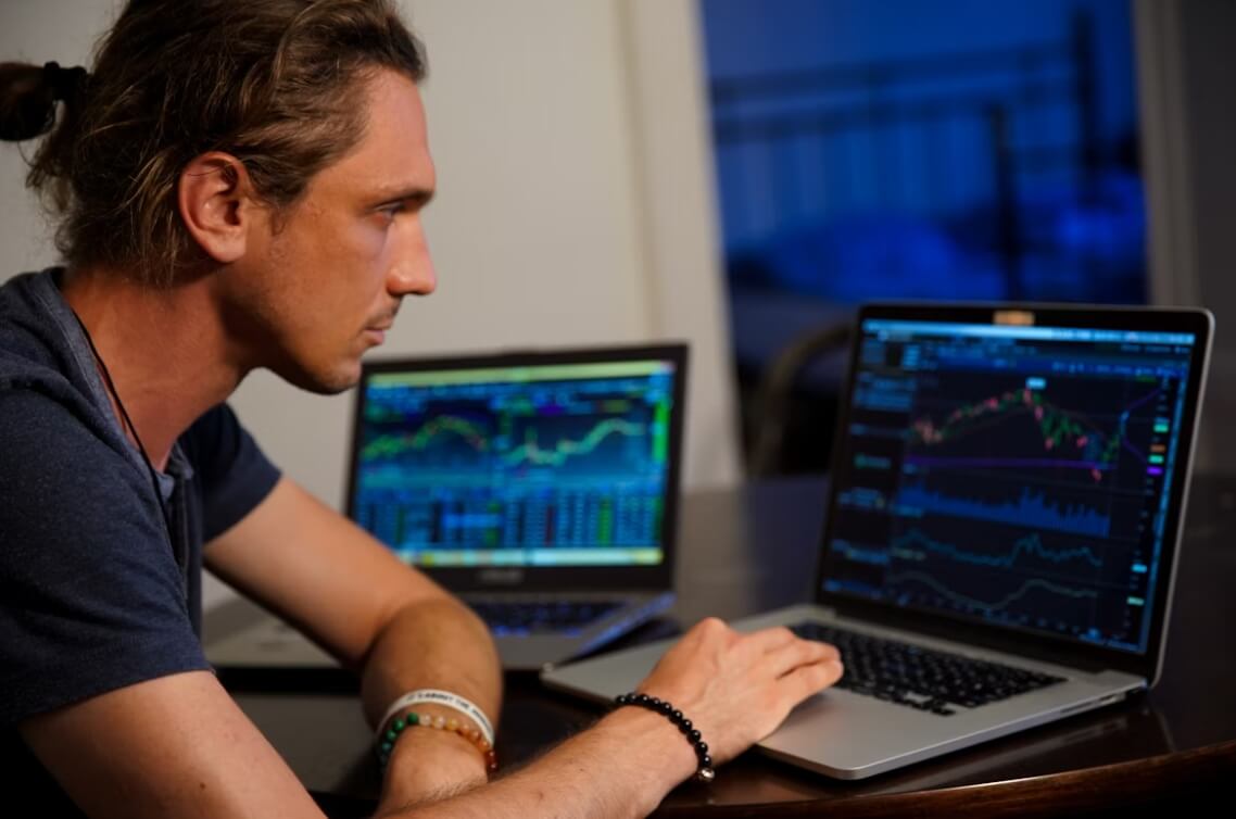 A man is studying trading charts on his laptop.